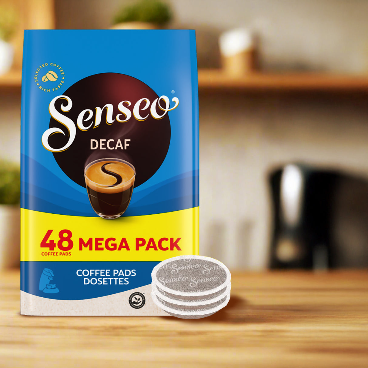 Senseo Decaf coffee pads package on a wooden surface with a blurred kitchen background