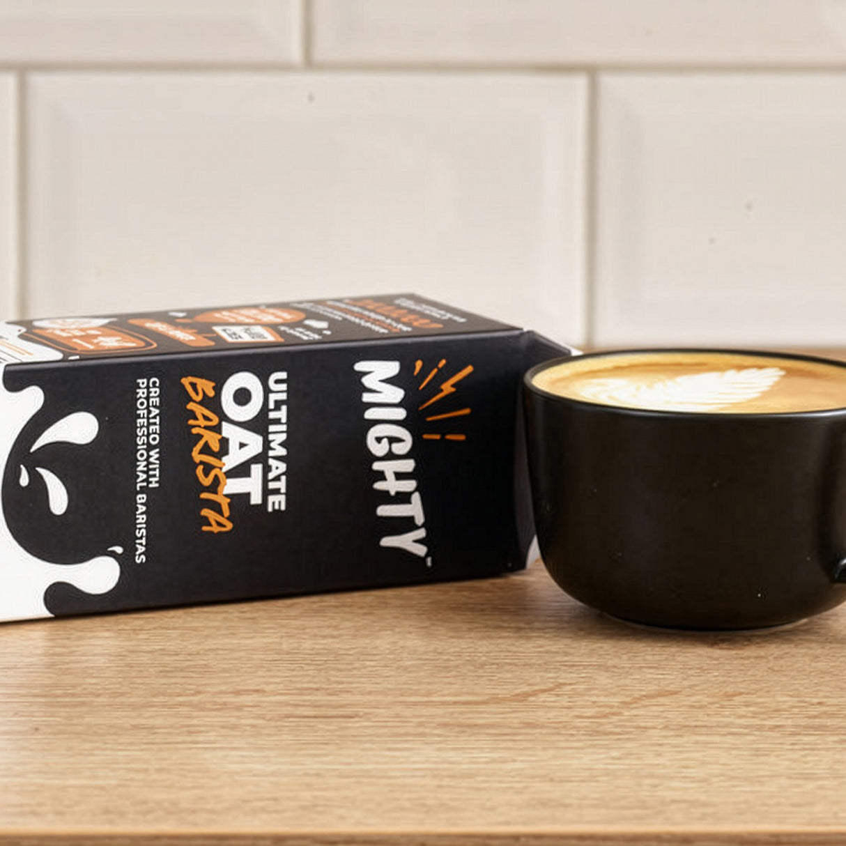 Mighty Oat Barista packaging with a black mug of oat milk latte on a wooden surface.