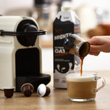 Person pouring coffee into a glass mug with a coffee machine and a carton of 'Mighty Oat' in the background.