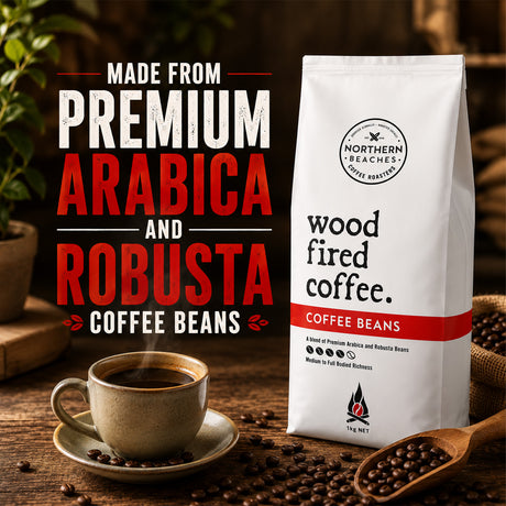 A bag of Northern Beaches Wood Fired Coffee Beans stands on a rustic wooden table beside a cup of black coffee, scattered coffee beans, a wooden spoon, and large promotional text reading 'Made from Premium Arabica and Robusta Coffee Beans.'.