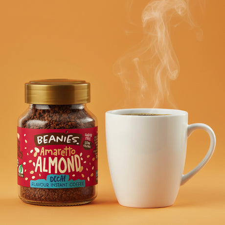 Jar of Beanies Amaretto Almond instant coffee and a steaming white mug on an orange background