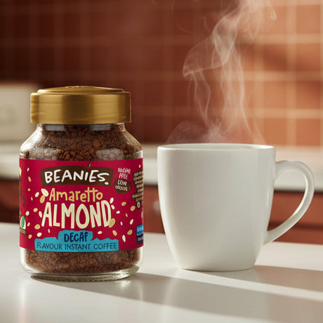 Jar of Beanies Amaretto Almond instant coffee with a steaming white mug on a table.