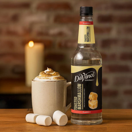 DaVinci Gourmet Toasted Marshmallow syrup bottle with a cup of hot chocolate and marshmallows on a wooden surface.