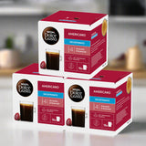 Two boxes of Dolce Gusto Americano Decaffeinated coffee capsules on a blurred kitchen background