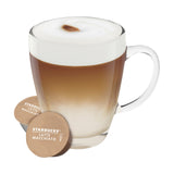 Clear mug with Starbucks Latte Macchiato coffee and two capsules on a white background