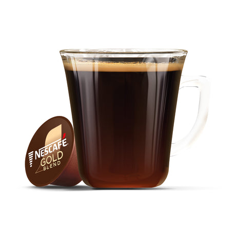 Glass mug filled with dark liquid next to a Nescafe Gold Blend capsule on a white background