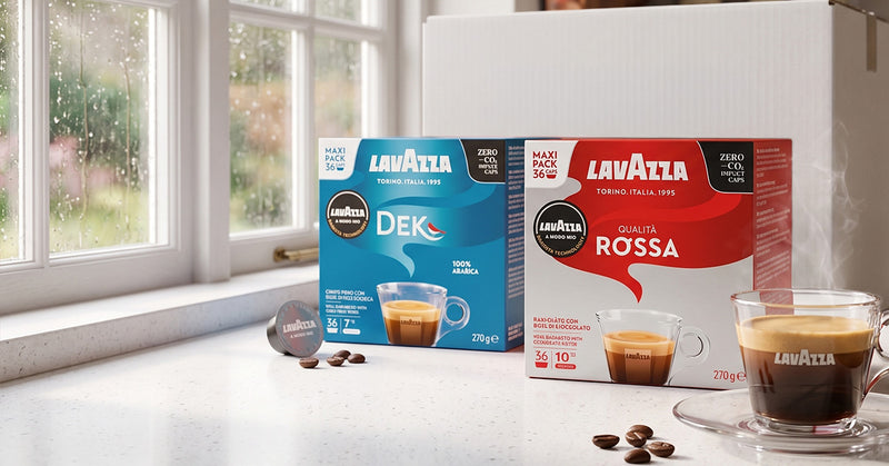 Two boxes of Lavazza coffee capsules, one blue DEK and one red ROSSA, displayed on a kitchen counter next to a window with raindrops, with espresso cups in the foreground.