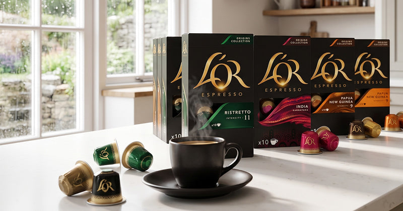 L'Or Espresso coffee capsules and their retail boxes arranged on a white countertop in a bright kitchen setting, with a black coffee cup and saucer in front.