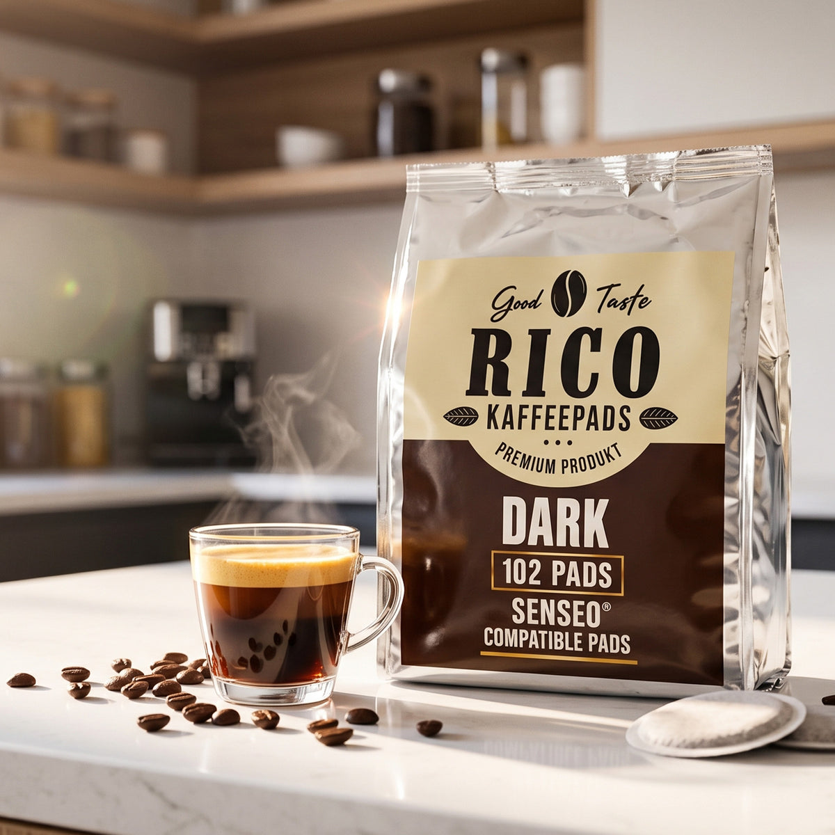 A bag of Rico Kaffepads Dark coffee filters stands on a kitchen counter next to a steaming glass cup of espresso, with scattered coffee beans and a spoon in a warm, blurred kitchen setting.
