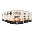 Six cans of Stormbrew Flat White coffee syrup arranged in a staggered row on a white background, with the center can fully visible and the cans fading slightly behind due to perspective.