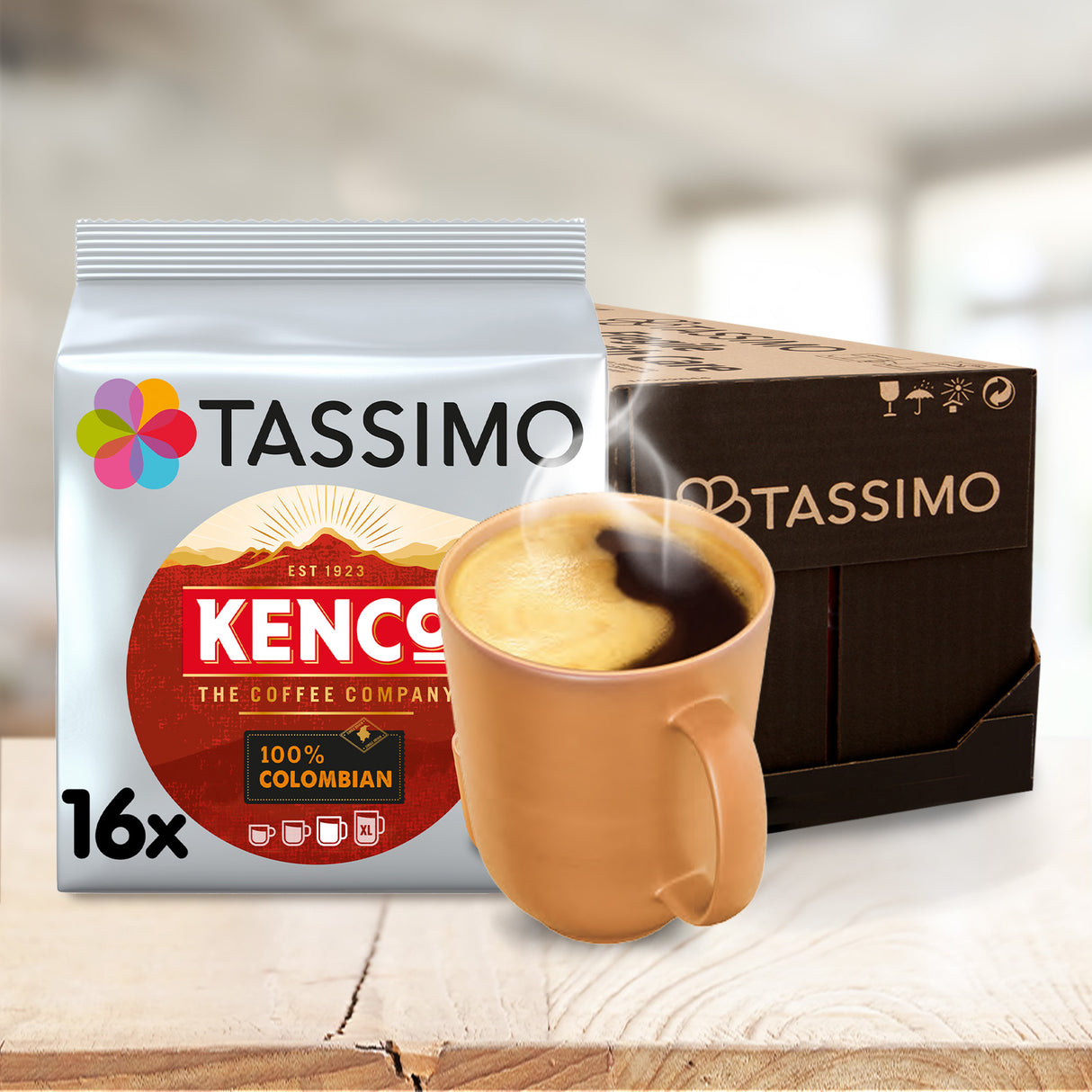 Tassimo Kenco Colombian coffee package with a steaming cup of coffee on a wooden surface.