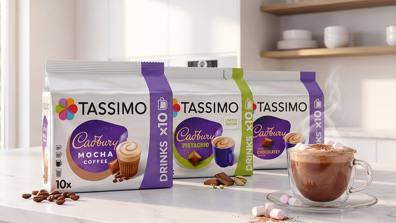 Tassimo Cadbury packs, Mocha, Pistachio, and Chocolate Berry flavors, displayed on a kitchen counter next to a cup of hot chocolate.