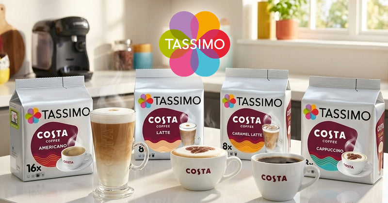 Four boxes of Tassimo Costa Coffee capsules arranged on a kitchen counter with matching coffee cups in front, including Americano, Latte, Caramel Latte, and Cappuccino. The Tassimo logo appears above the products, and a real kitchen environment is visible in the background.