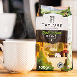 Taylors of Harrogate coffee bag with a steaming white mug on a wooden surface
