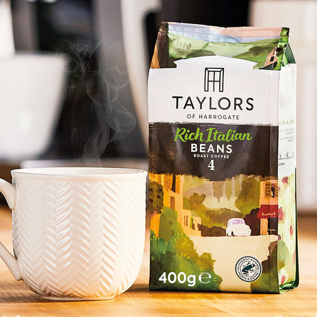 Taylors of Harrogate coffee bag with a steaming white mug on a wooden surface