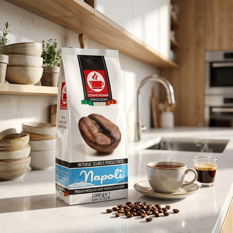 A bag of Espresso Roma Napoli coffee beans stands on a kitchen counter beside a cup of coffee, a glass of espresso, scattered coffee beans, and stacked ceramic bowls, with a blurred kitchen background.