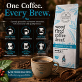 A bag of Northern Beaches Wood Fired Coffee Decaf Ground Coffee stands on a dark wooden surface beside a ceramic coffee cup, coffee beans, a spoon, and brewing-themed graphics. The package is white with light blue leaf illustrations and black text, while the cup is speckled beige with dark text.